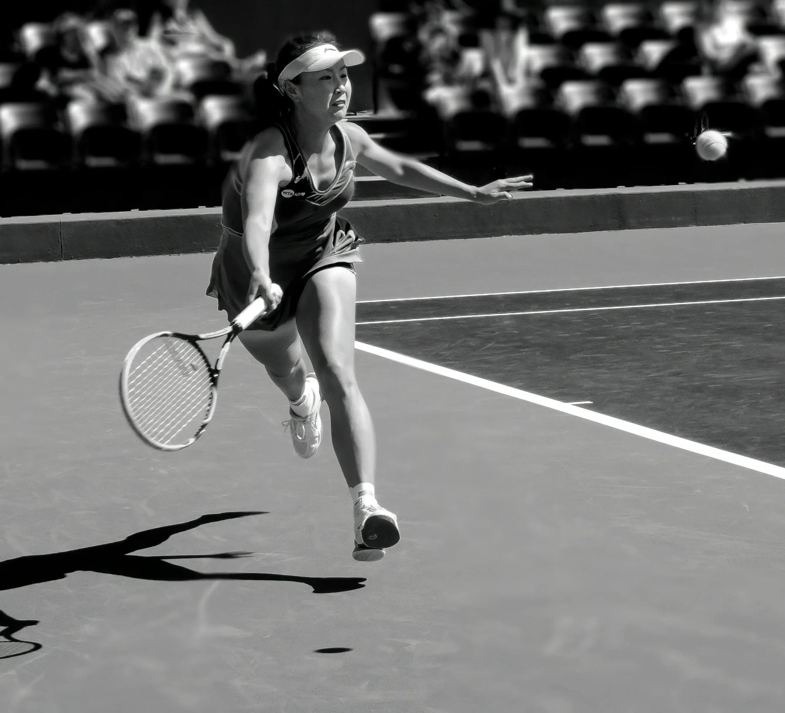 Black and white image of a female tennis player stretching for a shot, highlighting the dynamic movement and physical conditioning central to Evolve's science based tennis training and player development.