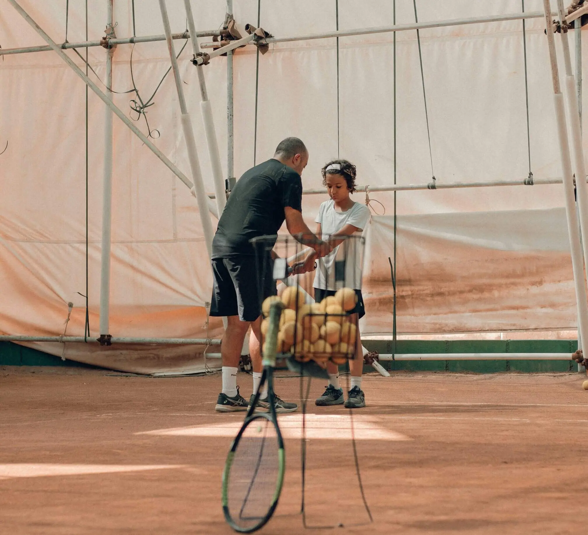 Tennis coach working with a young player on court, illustrating the practical application of skills learned through tennis coach development and tennis coach workshops for effective training.