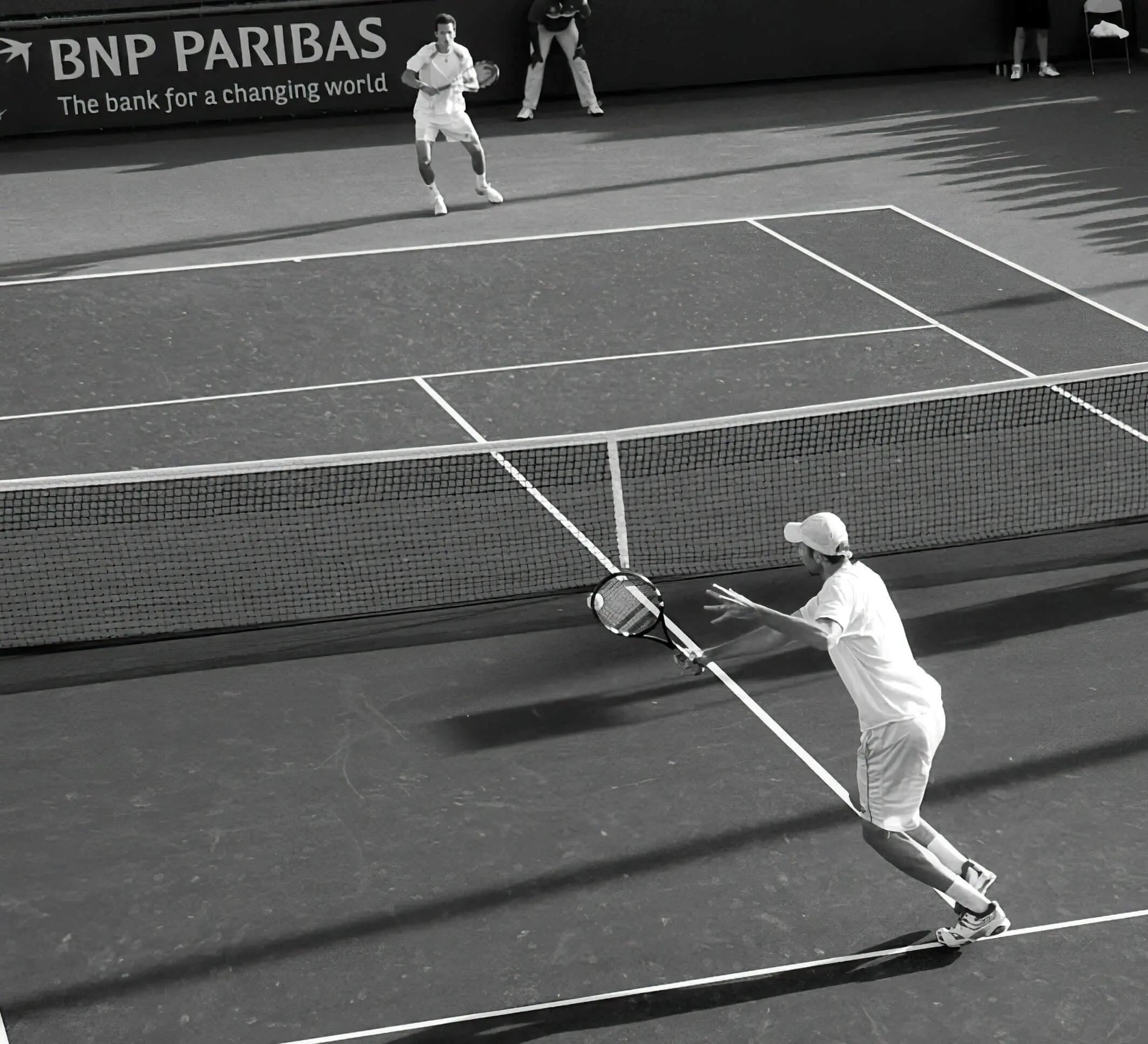 Black and white image of two tennis players competing on a court, illustrating the results of dedicated tennis player development and science based tennis training.